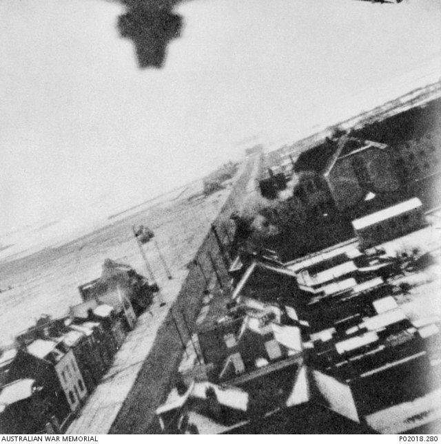 Black-and-white wartime aerial photograph of Amiens prison during the 18 February 1944 raid, with a Mosquito aircraft visible above the compound.