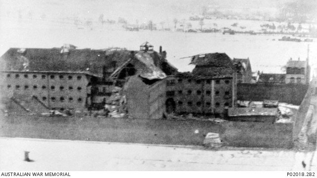 Black-and-white photograph of bomb damage and a large breach in the wall of Amiens prison after the February 1944 raid.