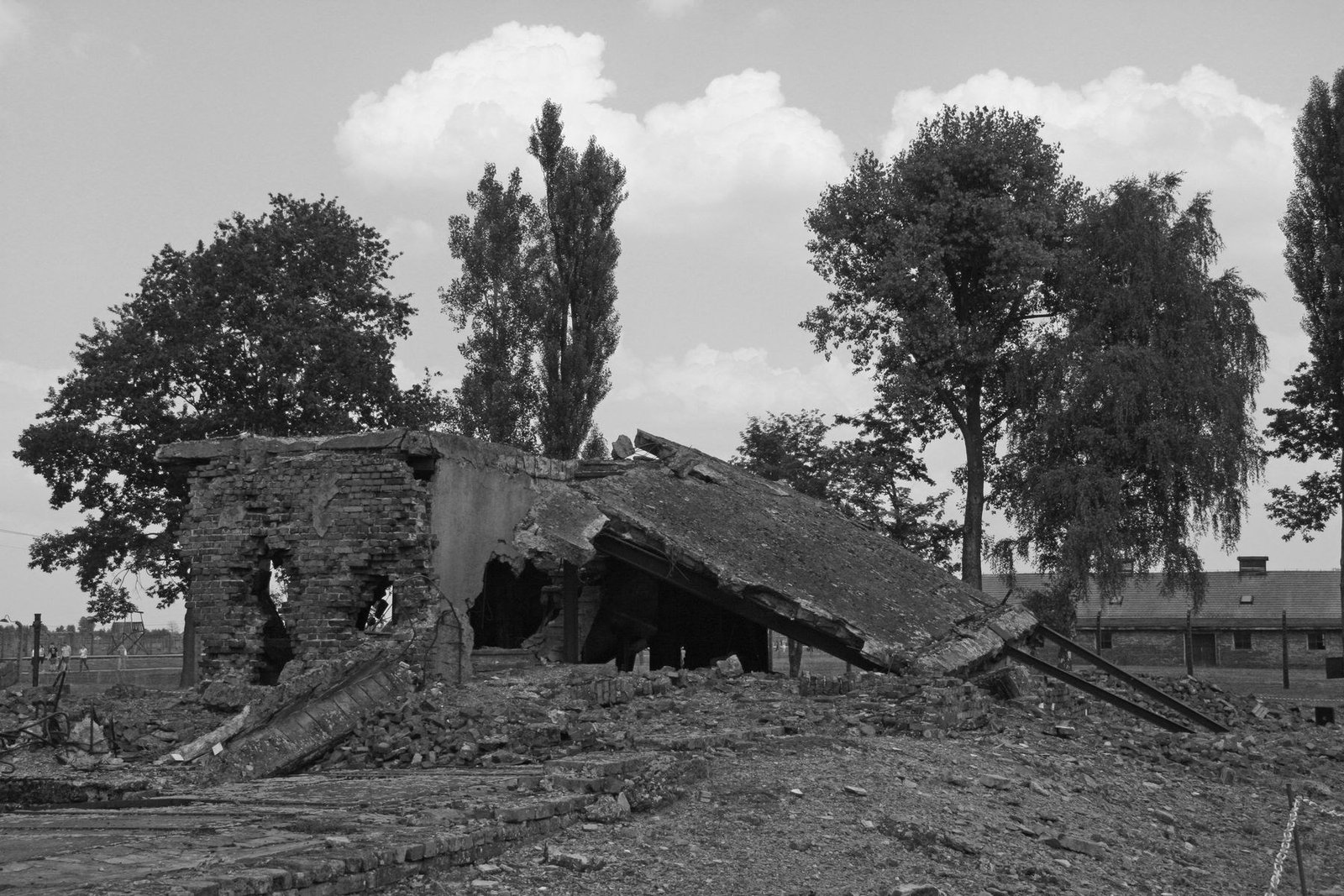Ruins of Crematorium IV at the Auschwitz-Birkenau memorial site, with collapsed masonry surrounded by trees and surviving camp structures.